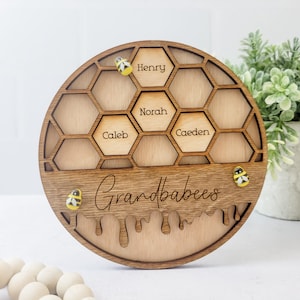 May include: Wooden honeycomb-shaped sign with the names Henry, Norah, Caleb, and Caeden in each cell. The sign says "Grandbabees" at the bottom with a dripping honey design and three yellow and black bees.