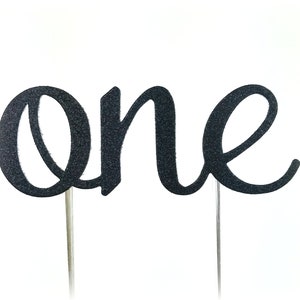 May include: Black glitter cake topper with the word "one" in a cursive font.