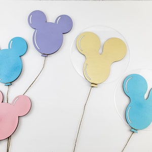 K&ouml;nnte beinhalten: F&uuml;nf Mickey-Maus-f&ouml;rmige Ballons aus Holz in verschiedenen Farben. Die Ballons h&auml;ngen an Schn&uuml;ren. Die Ballons sind hellblau, lila, gelb und zwei sind blau.