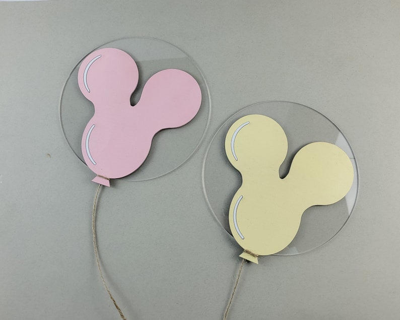 K&ouml;nnte beinhalten: Zwei transparente Acryl-Anh&auml;nger in Form von Mickey-Maus-Ohren. Ein Anh&auml;nger ist rosa und der andere ist gelb.