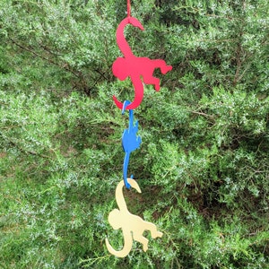 Puede incluir: Tres siluetas de monos colgantes, una roja, una azul y una amarilla, sobre un fondo verde de hojas.