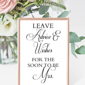 May include: A white sign with a rose gold frame that says "Leave Advice & Wishes for the Soon to be Mrs."