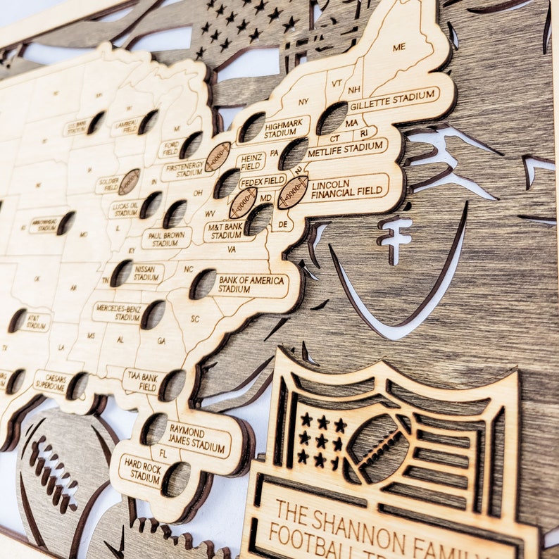 K&ouml;nnte beinhalten: Holzkarte der USA mit Namen von Footballstadien, lasergeschnitten. Die Karte zeigt das NFL-Logo, Fu&szlig;b&auml;lle und den Text "The Shannon Family Football Trip".