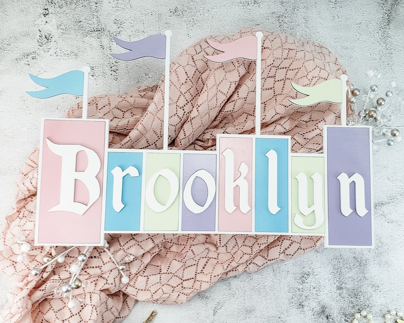 May include: A wooden castle-shaped sign with the name "Brooklyn" spelled out in white letters on pastel-colored panels. The sign is decorated with colorful flags.