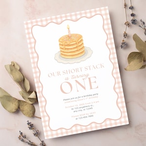 Puede incluir: Una invitación de cumpleaños con una ilustración de acuarela de una pila de panqueques con una vela encendida. La invitación tiene un borde rosa a cuadros y el texto "OUR SHORT STACK is turning ONE".
