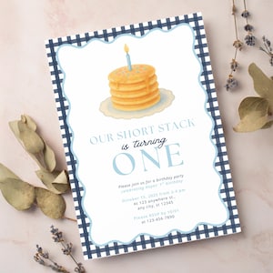 May include: A birthday invitation featuring a stack of pancakes with a candle, set against a blue gingham border. The text reads "OUR SHORT STACK is turning ONE". The invitation is for a first birthday.