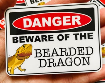 May include: A rectangular sticker with a black border and the words "DANGER" in a red oval. The text "BEWARE OF THE BEARDED DRAGON" is below, with a cartoon bearded dragon illustration.
