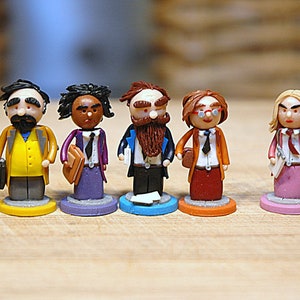 May include: Five miniature figurines of people wearing business attire. The figurines are made of clay and are painted in various colors, including yellow, purple, blue, orange, and pink. The figurines are standing on small round bases.