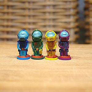 May include: Four small, colorful figurines of astronauts wearing helmets. The astronauts are standing on round bases. The astronauts are painted in shades of blue, green, yellow, and purple.