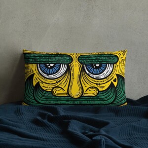 May include: A yellow and green pillow with a cartoon face printed on it. The face has blue eyes, a yellow nose, and a green mustache.