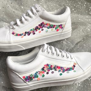 May include: White canvas low-top sneakers with a colorful sequin design on the side. The sequins are arranged in a wave pattern.