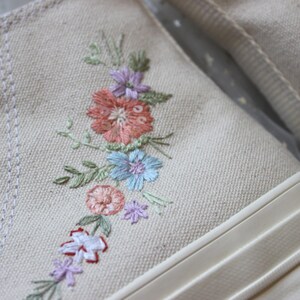 May include: A pair of white canvas high-top sneakers with embroidered flowers in shades of pink, blue, and green.