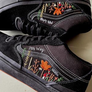May include: Black Vans sneakers with embroidered floral designs in orange, green, and red. The text "mr Way" is embroidered on the side. The shoes have black soles and white stitching. The brand name "Vans" is visible.