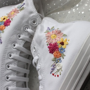 May include: White canvas high-top sneakers with embroidered floral designs in shades of pink, yellow, orange, blue, and green.