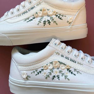 May include: White canvas sneakers with floral embroidery. The sneakers feature embroidered flowers and greenery in shades of cream and green. One shoe has "Mrs Green" embroidered on the side, and the other has the date "01.05.2026".