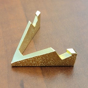 Puede incluir: Un soporte de exhibición de metal dorado con forma triangular y superficie texturizada.