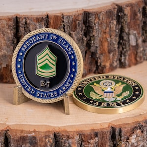May include: A gold-colored coin with a blue and black border, featuring the text "SERGEANT 1ST CLASS" and "UNITED STATES ARMY". The coin displays the rank insignia of an E-7 Sergeant. Another coin with the US Army emblem is also visible.