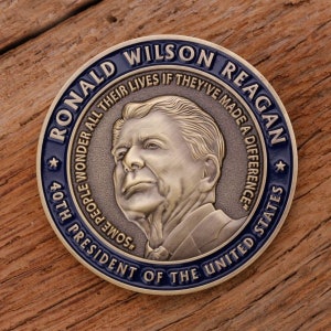 May include: A commemorative coin featuring Ronald Wilson Reagan, the 40th President of the United States. The coin has a bronze finish with a blue border. Text includes "RONALD WILSON REAGAN" and "SOME PEOPLE WONDER ALL THEIR LIVES IF THEY'VE MADE A DIFFERENCE."