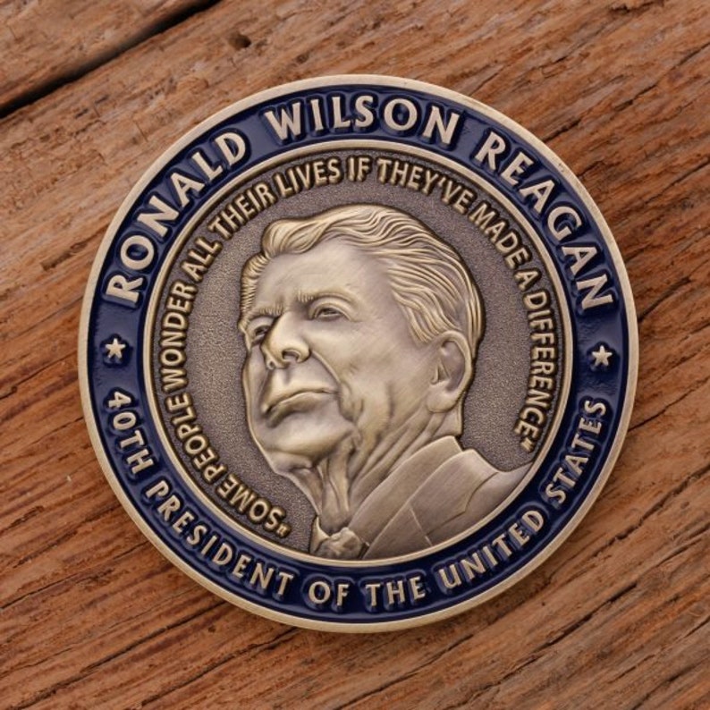 May include: A commemorative coin featuring Ronald Wilson Reagan, the 40th President of the United States. The coin has a bronze finish with a blue border. Text includes "RONALD WILSON REAGAN" and "SOME PEOPLE WONDER ALL THEIR LIVES IF THEY'VE MADE A DIFFERENCE."