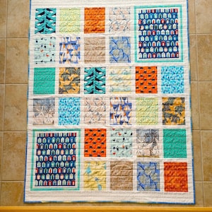 May include: A white quilt with a blue, green, and orange patchwork design. The quilt is made up of squares with different patterns, including seashells, sailboats, and houses.