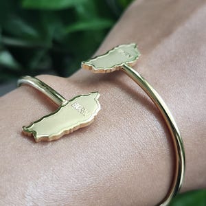 Puede incluir: Pulsera de oro con dos dijes en forma de la isla de Puerto Rico. Los dijes están grabados con "BORIN" y "GUAYNA".