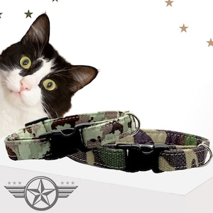 May include: Two pet collars featuring a green, brown, and black camouflage pattern. Each collar includes a black plastic side-release buckle and a silver-toned metal D-ring for attaching tags. The fabric has visible stitching along the edges.
