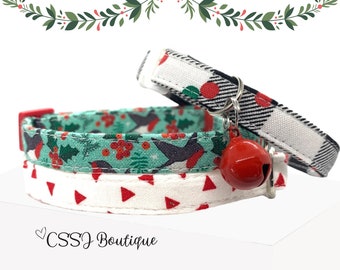 May include: Three festive cat collars with holiday patterns. One collar features a red and white buffalo check, another has a teal background with birds and holly, and the third has a white background with red triangles. A red bell hangs from one collar.