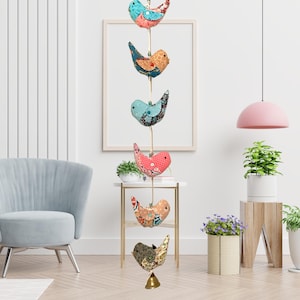 May include: A string of five colorful fabric birds hanging from the ceiling. The birds are in shades of blue, pink, and orange with floral patterns. The birds are hanging from a white string with a bell at the bottom.