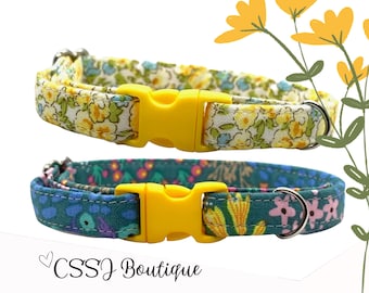 May include: Two adjustable cat collars with floral patterns. The top collar has a white background with yellow and blue flowers. The bottom collar has a green background with yellow, pink, and blue flowers. Both collars have yellow plastic buckles and silver D-rings.