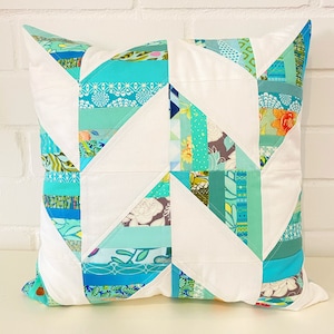 Könnte beinhalten: Ein weißes Kissen mit einem geometrischen Muster aus aquablauen und türkisfarbenen Stoffresten. Das Kissen ist im Patchwork-Stil gefertigt und hat einen weißen Hintergrund.