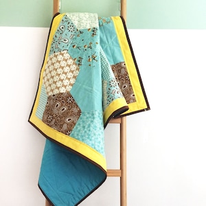 Può includere: Una trapunta patchwork turchese e marrone con bordatura gialla è drappeggiata su una scala di legno.