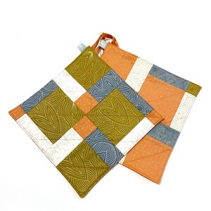 Könnte beinhalten: Zwei gequiltete Topflappen, einer mit einem geometrischen Muster in Orange-, Weiß- und Blautönen, der andere mit einem wirbelnden Muster in Grün-, Weiß- und Blautönen.