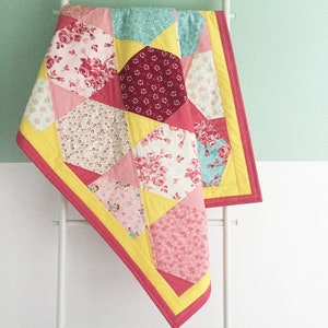 Könnte beinhalten: Eine rosafarbene und gelbe Patchwork-Decke mit Blumenmuster. Die Decke hängt an einer weißen Leiter vor einer hellgrünen Wand.