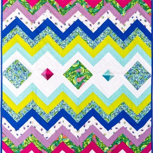 Può includere: Una trapunta colorata e fatta a mano con un vivace motivo a zig-zag. La trapunta presenta zig-zag nelle tonalità di rosa, blu, verde, giallo e bianco. Forme geometriche a diamante sono centrate sulla trapunta. La trapunta è bordata con un bordo blu.