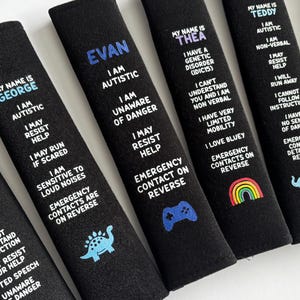 May include: Six black rectangular seat belt covers featuring personalized names in colored text and white printed information regarding medical conditions, autism, and safety instructions, with small graphic icons like a dinosaur, game controller, rainbow, and elephant.