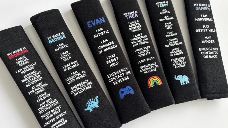 May include: Six black rectangular seat belt covers featuring personalized names in colored text and white printed information regarding medical conditions, autism, and safety instructions, with small graphic icons like a dinosaur, game controller, rainbow, and elephant.