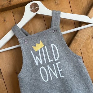 May include: Grey baby dungarees with a white crown and the text "WILD ONE" in white.