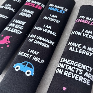 May include: Four black rectangular seat belt covers featuring white printed text and colorful icons. Each cover displays a name in pink or blue, followed by specific medical or behavioral information such as autism, ADHD, allergies, and non-verbal status.