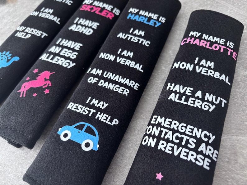 May include: Four black rectangular seat belt covers featuring white printed text and colorful icons. Each cover displays a name in pink or blue, followed by specific medical or behavioral information such as autism, ADHD, allergies, and non-verbal status.