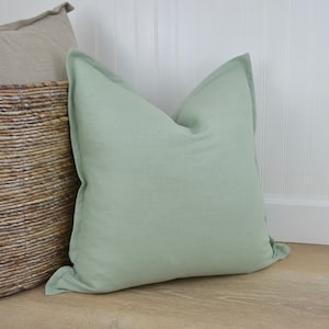 May include: A soft, light green throw pillow with a simple, rectangular shape. The pillow is made of a linen fabric and has a subtle texture.