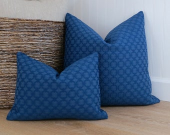 Op de afbeelding: Twee blauwe kussens met een cirkelvormig patroon op een lichte houten vloer. De kussens zijn gemaakt van een zachte, textuurrijke stof.
