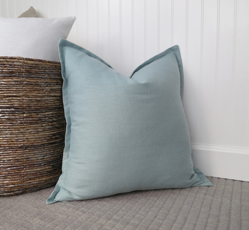 May include: A light blue square pillow with a subtle texture. The pillow is sitting on a gray textured surface.
