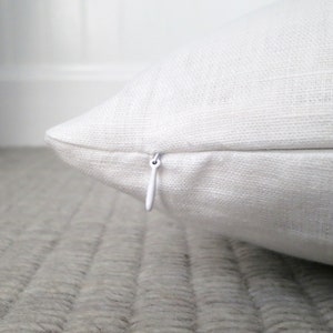 Close up view of the bright white linen pillow showing the hidden zipper enclosure for the pillow cover and detail of the linen fabric.