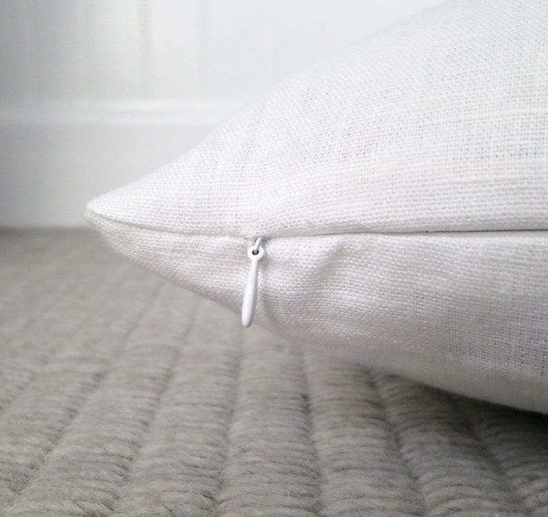 Close up view of the bright white linen pillow showing the hidden zipper enclosure for the pillow cover and detail of the linen fabric.
