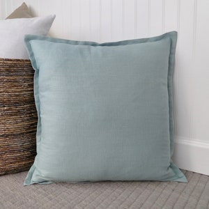 May include: A light blue square throw pillow with a subtle linen texture. The pillow is sitting on a gray carpet.