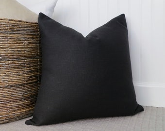 May include: A black linen pillow with a simple design. The pillow is sitting on a light gray rug.