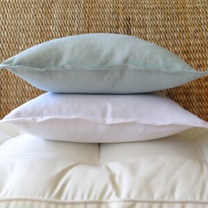 May include: Two decorative pillows, one white and one light blue, are stacked on top of each other. The pillows are made of a soft, textured fabric.