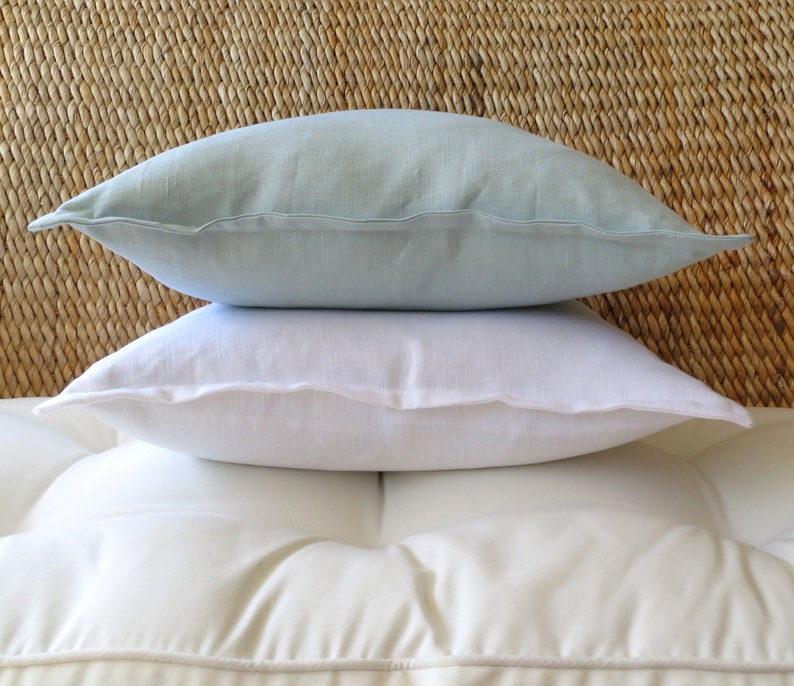 May include: Two decorative pillows, one white and one light blue, are stacked on top of each other. The pillows are made of a soft, textured fabric.