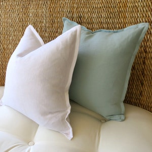 May include: Two decorative throw pillows, one white and one light blue, are placed on a white couch with a woven wicker headboard.