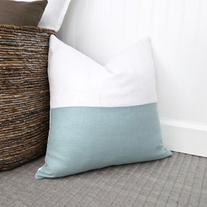May include: A white and light blue pillow with a simple design. The pillow is made of a soft, textured fabric.